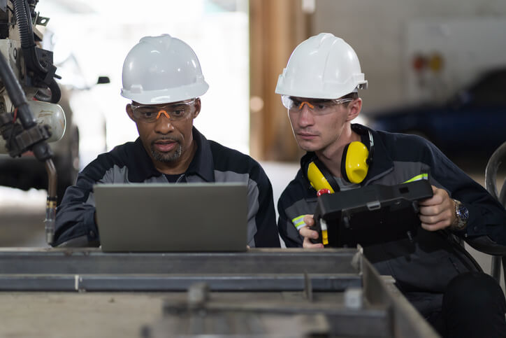 Two welders reading the blueprint of a structure on a tab during welder training