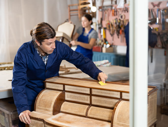 A Cabinetmaker sanding a dresser according to cabinet-making courses