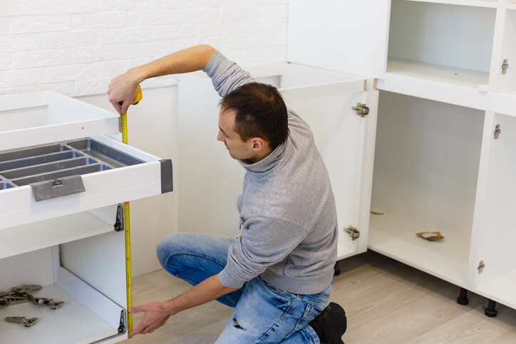 A cabinet maker taking measurements of a kitchen cabinet after completing cabinet making training