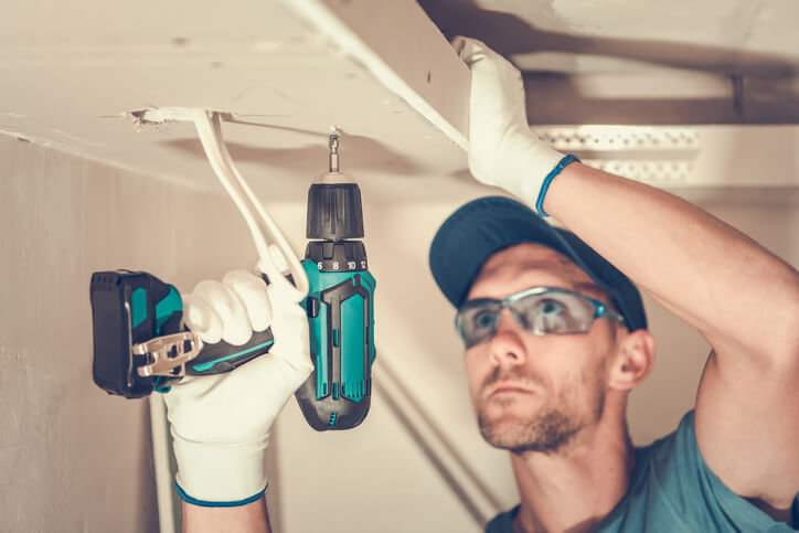A professional Drywall Installer working on a ceiling after home renovation training.