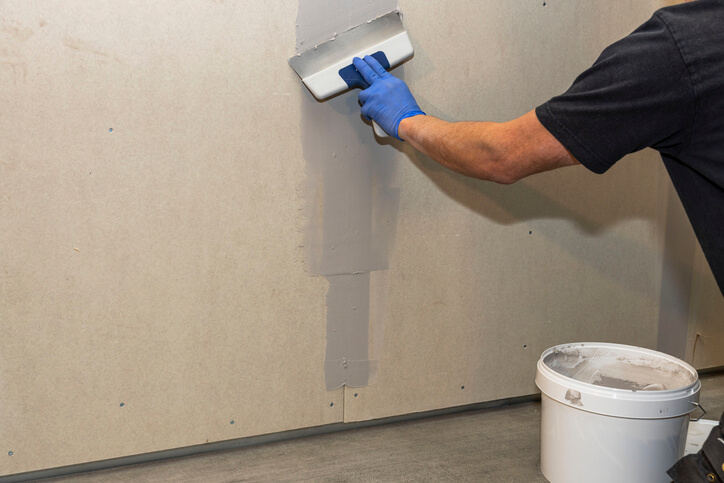 After home renovation training, a male Drywall Installer working on a wall in a renovated building.