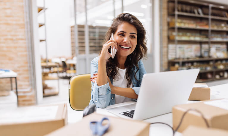 A logistics management training graduate working at a desk and speaking over the phone.