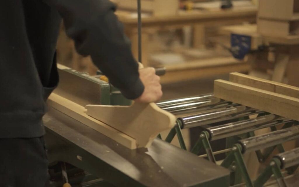 A close-up of a person's hands using a jointer to smooth a piece of wood, which is part of the practical skills acquired during cabinetmaking training