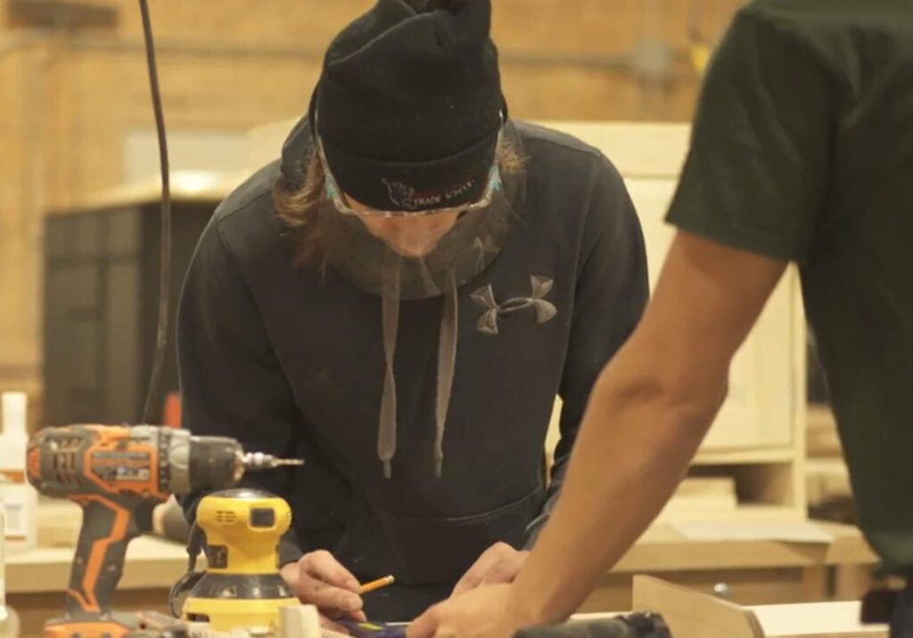 A focused cabinet making student laying out measurements on a wooden board