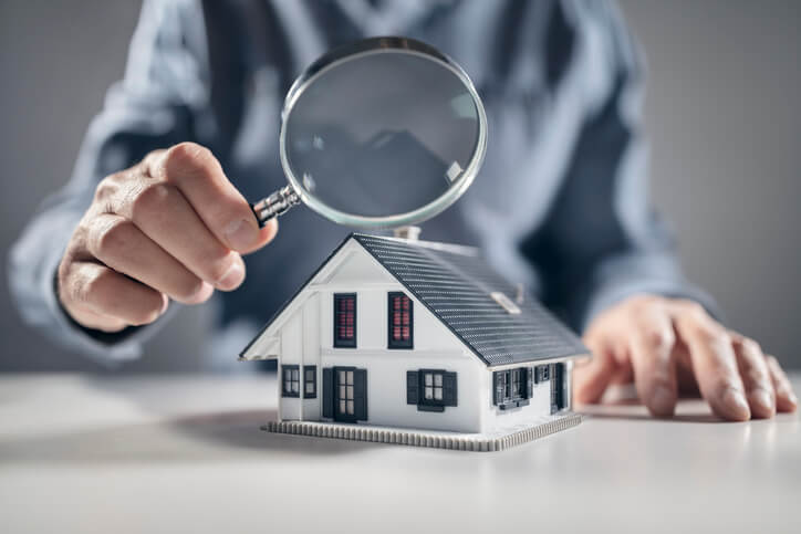 A man holding a magnifying glass over a house model in home inspection training