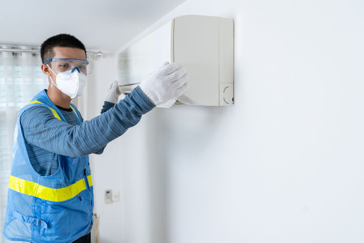 An HVAC training technician graduate wearing applicable PPE to diagnose and fix air conditioner issues.